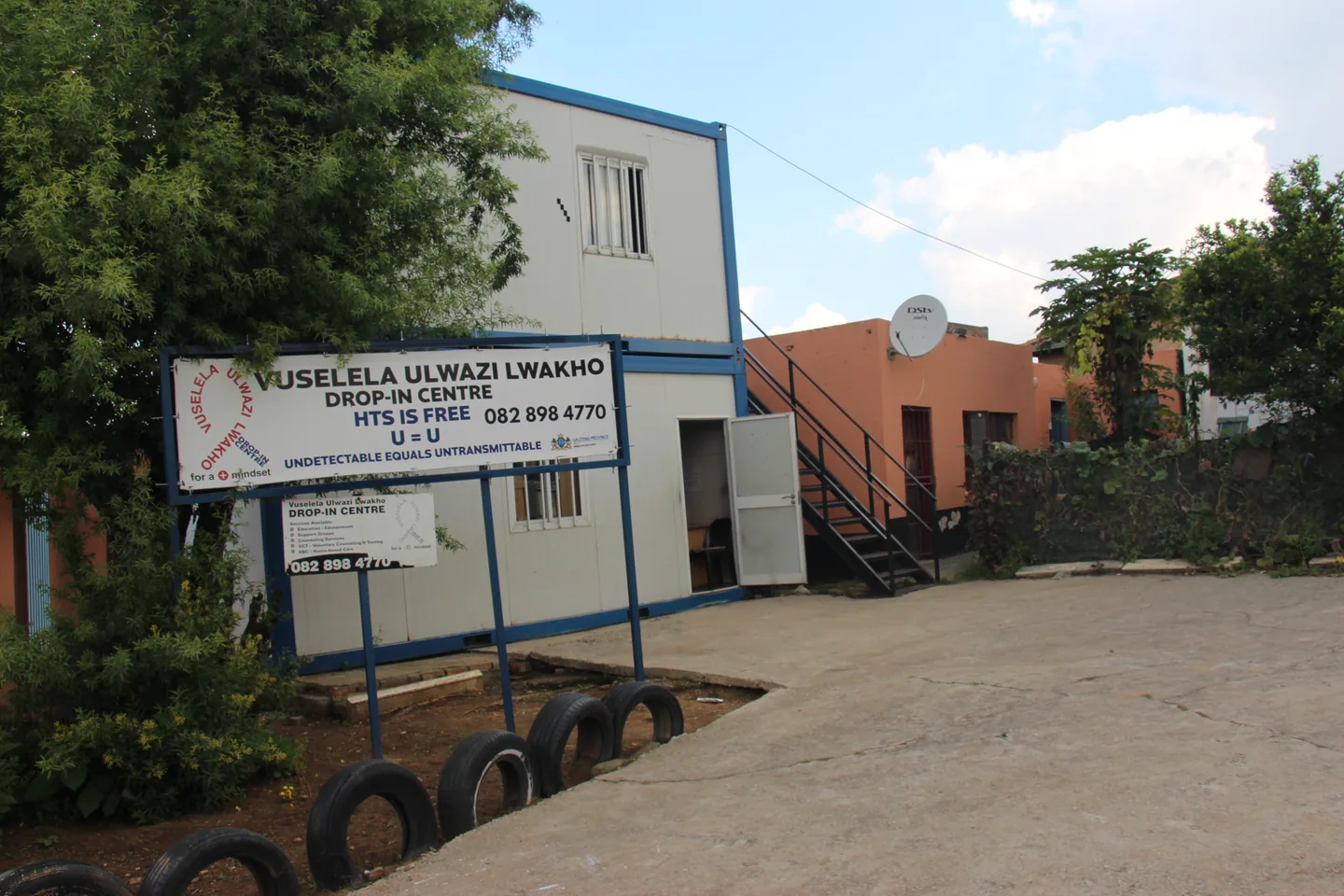 Two-storey portable building with an outdoor staircase, a Vuselela sign and surrounding trees.