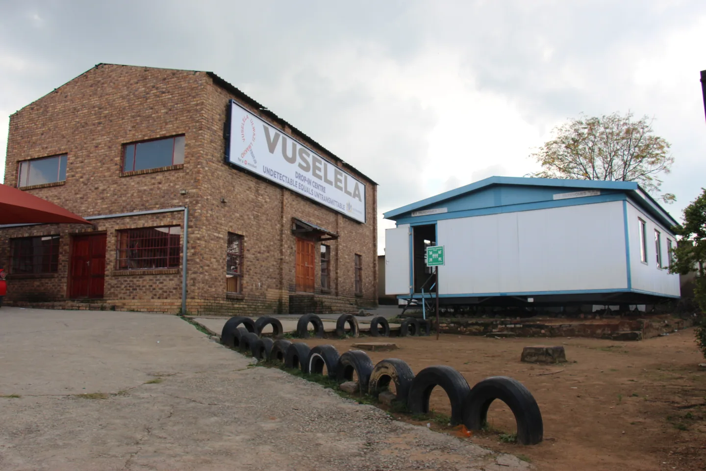 Brick Vuselela building beside a white portable building and a tyre-lined courtyard.