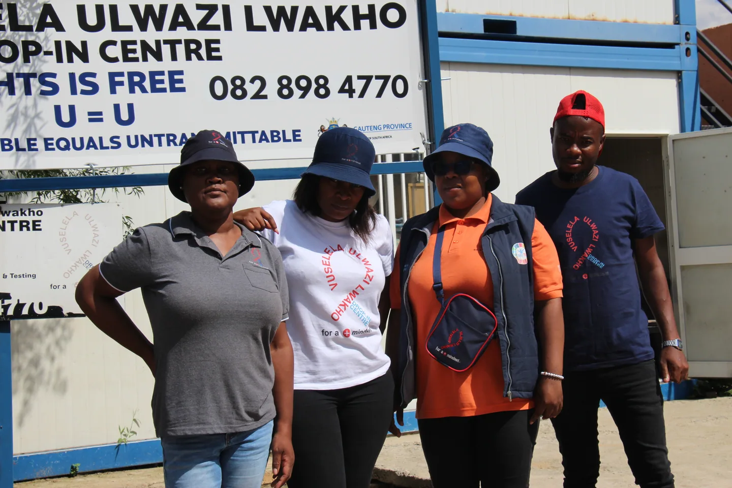Four people posing beside a Vuselela sign in branded shirts and hats.